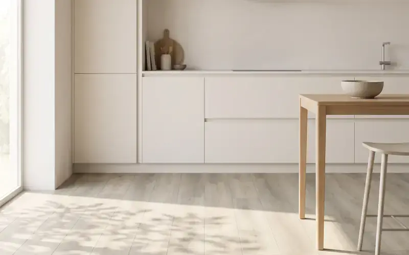 Light grey oak plank floor in a bright kitchen with white flat-front cabinets and a wood table