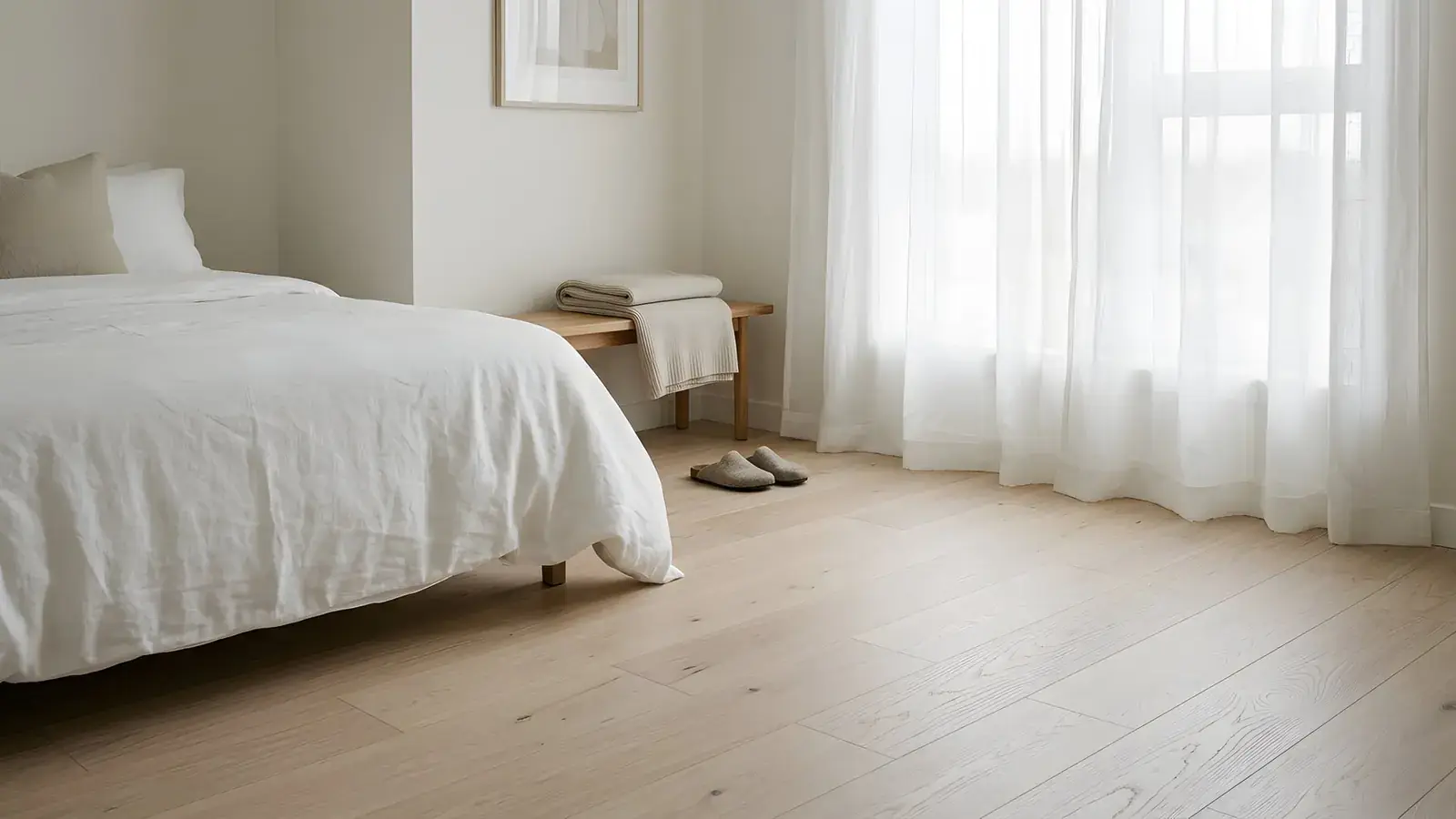 Pale wide-plank oak floor in a quiet bedroom with white linen bedding and sheer curtains