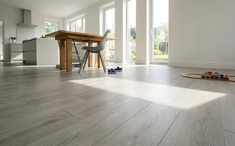 Grey oak-look plank floor in a bright open kitchen and dining room with a toy train track by the wall