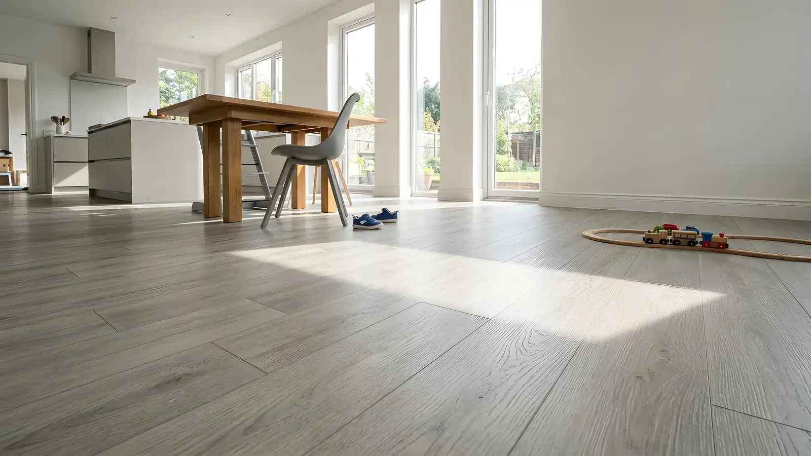 Grey oak-look plank floor in a bright open kitchen and dining room with a toy train track by the wall