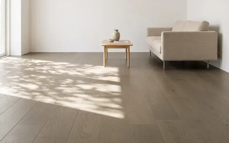 Wide taupe oak plank floor in a sunlit living room with a linen sofa and a small wood side table