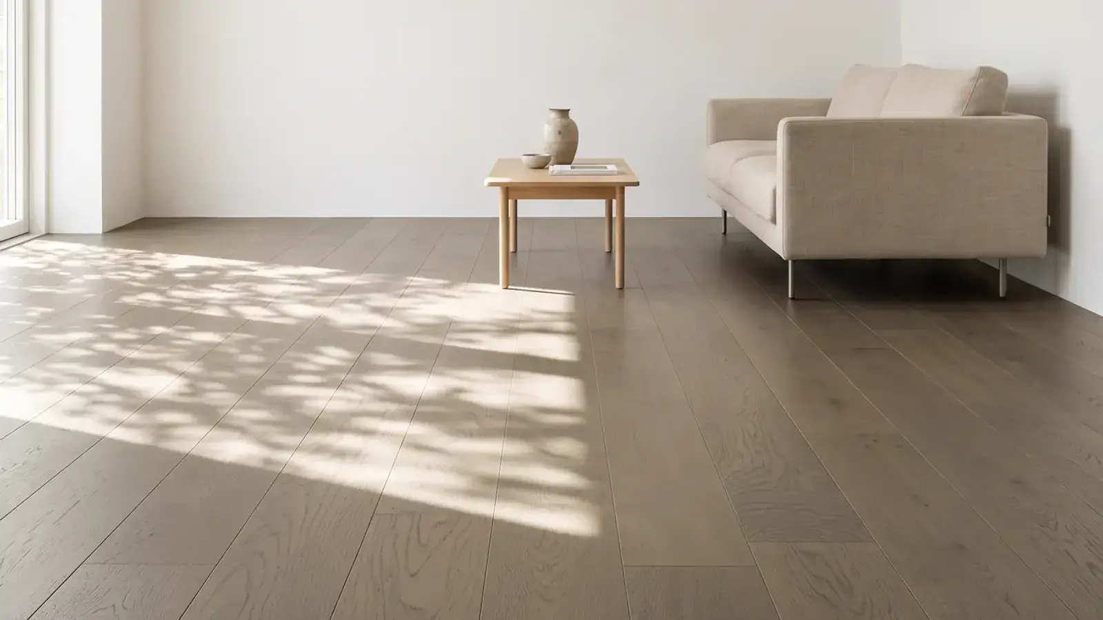 Wide taupe oak plank floor in a sunlit living room with a linen sofa and a small wood side table