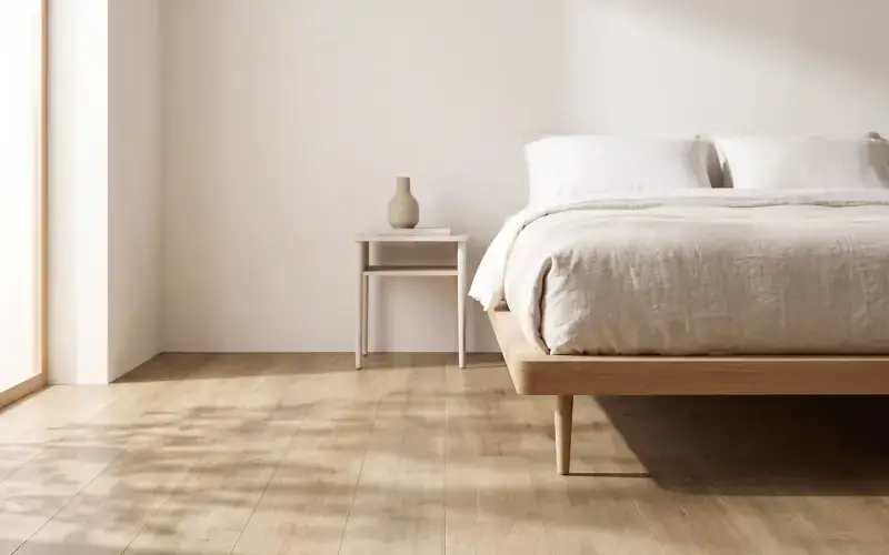 Bedroom with natural oak plank flooring, a low wooden bed frame in linen bedding and a small side table