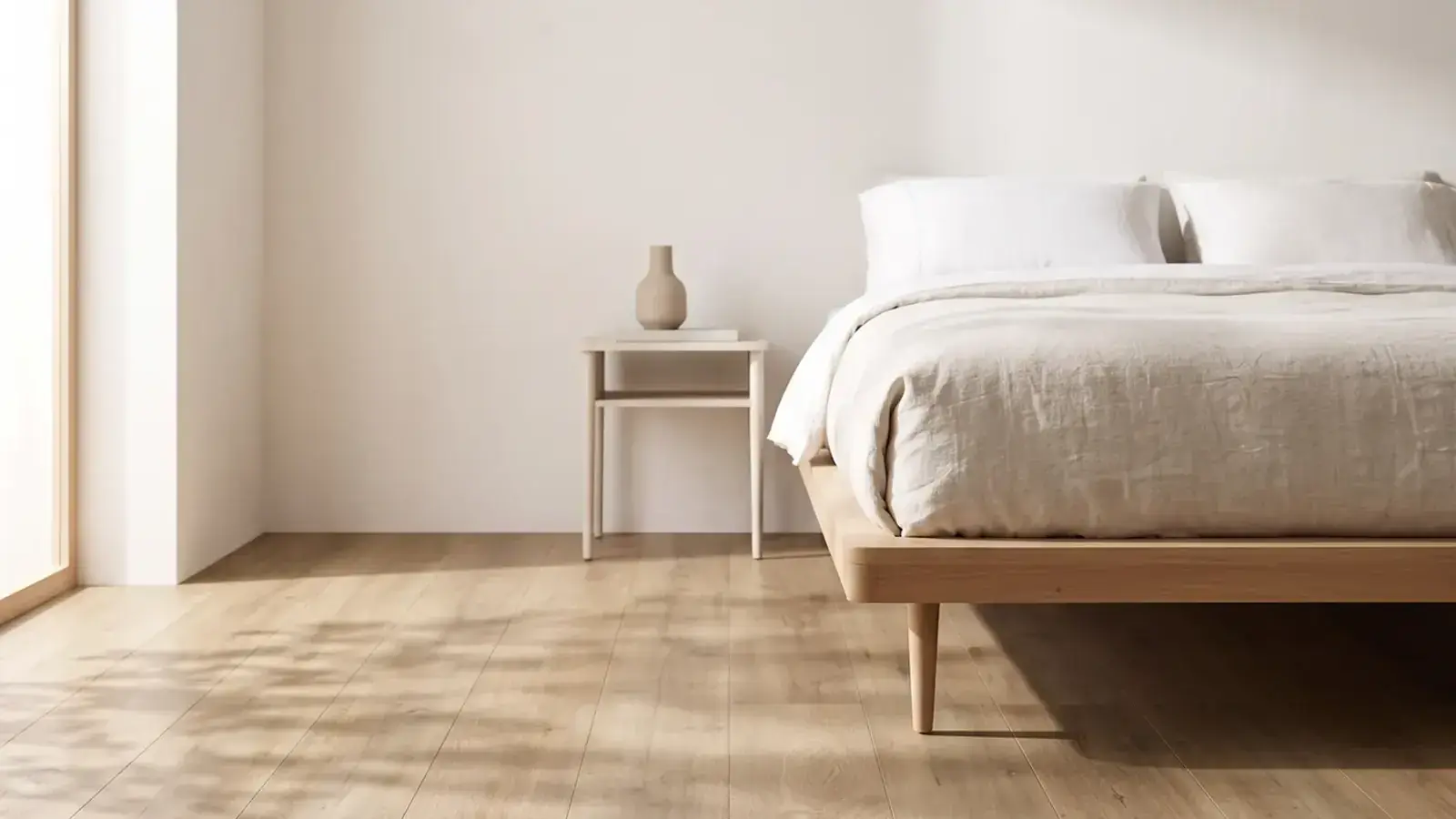 Bedroom with natural oak plank flooring, a low wooden bed frame in linen bedding and a small side table